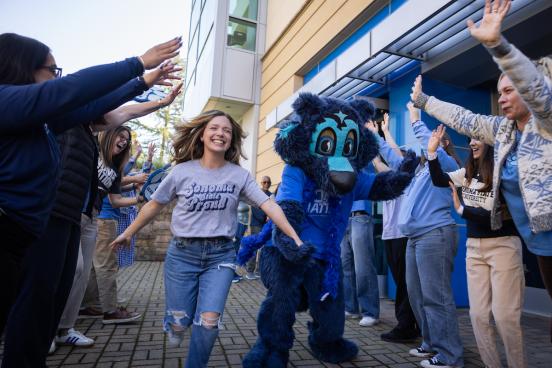 Student running with Lobo with a group of people with their arms in the air cheering them on